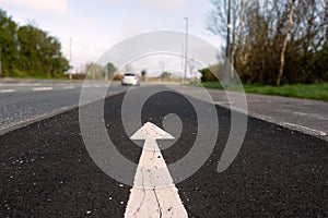 White arrow on a black asphalt surface in focus, moving car out of focus in th background. Selective focus. Direction sign on a