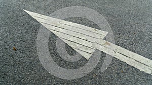 A white arrow painted sign on a gray paved road pointing the direction the car was supposed to drive