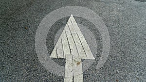 A white arrow painted sign on a gray paved road pointing the direction the car was supposed to drive