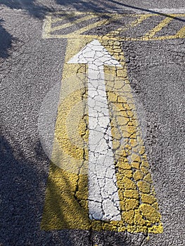 White arrow on a yellow background on cracked road tarmac