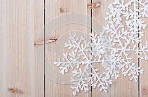 White artificial snowflakes on a light wooden table. Christmas decoration background and copy space for text. Closeup.