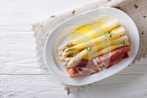 White asparagus with hollandaise sauce and ham close-up on a plate. Horizontal top view