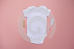 White baby bodysuit on a baby pink background with IVF letters and ovulation thermometer