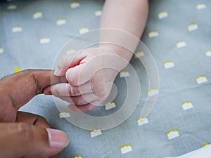 White baby holding finger of black adult hand