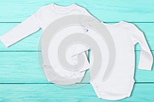 White baby mock up jumpsuit on blue wooden background. Baby bodysuit mockup and template blank copy space. Top view. One-piece