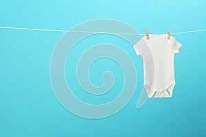 White baby onesie hanging on clothes line against blue background. Laundry day photo