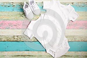 White baby onesie and sneakers over pastel wooden background. Good for insert your design. Mock up.