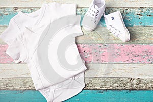 White baby onesie and sneakers over pastel wooden background. Good for insert your design. Mock up.