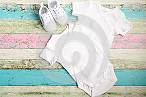 White baby onesie and sneakers over pastel wooden background. Good for insert your design. Mock up. photo