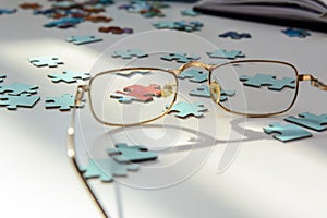 On a white background blue puzzles. A red puzzle is visible through the lens of the glasses. photo