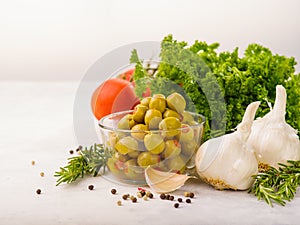 On a white background, a bowl with green olives, herbs, tomatoes, garlic, black peppercorns. Organic vegetarian food. Healthy food