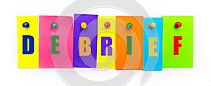 On a white background, buttons are used to fix bright multi-colored strips of paper with the text DEBRIEF photo