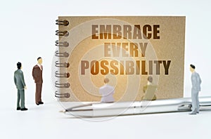 On a white background, figures of businessmen, a pen and a notepad with the inscription - Embrace Every Possibility