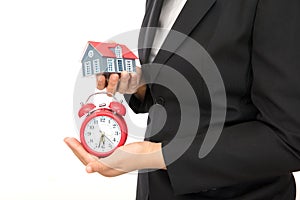 White background front dress female staff holding alarm clock and small house model