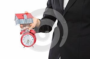 White background front dress female staff holding alarm clock and small house model