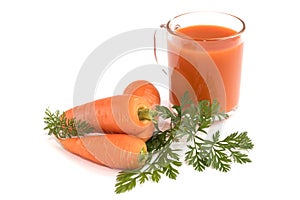 On an  white background, a full glass of fresh carrot juice and a whole carrot with leaves.