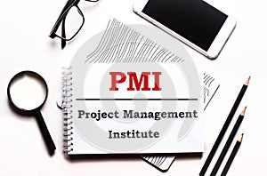 On a white background glasses, a magnifier, pencils, a smartphone and a notebook with the text PMI Project Management Institute