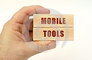 On a white background, a hand that holds wooden blocks with the inscription - Mobile Tools