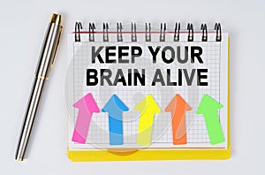 On a white background lie a pen and a notebook with the inscription - KEEP YOUR BRAIN ALIVE