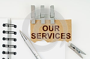 On a white background lies a notebook, a pen, clothespins and cardboard with the inscription - Our Services