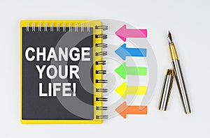 On a white background lies a pen, arrows and a notebook with the inscription - CHANGE YOUR LIFE