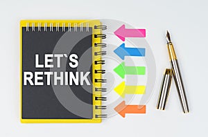 On a white background lies a pen, arrows and a notebook with the inscription - LETS RETHINK