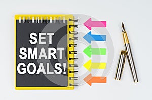On a white background lies a pen, arrows and a notebook with the inscription - SET SMART GOALS