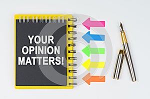 On a white background lies a pen, arrows and a notebook with the inscription - YOUR OPINION MATTERS