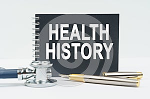 On a white background lies a stethoscope, a pen and a black notebook with the inscription - HEALTH HISTORY