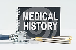 On a white background lies a stethoscope, a pen and a black notebook with the inscription - MEDICAL HISTORY