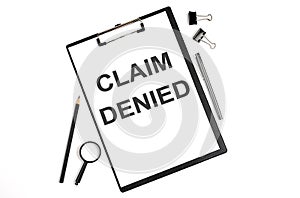 On a white background magnifier, a pen and a sheet of paper with the text CLAIM DENIED. Business concept
