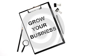 On a white background magnifier, a pen and a sheet of paper with the text GROW YOUR BUSINESS . Business concept