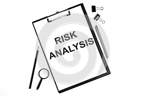 On a white background magnifier, a pen and a sheet of paper with the text RISK ANALYSIS . Business concept