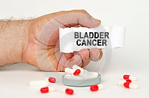 On a white background, medical capsules, in the hands of a person a paper plate with the inscription - Bladder cancer