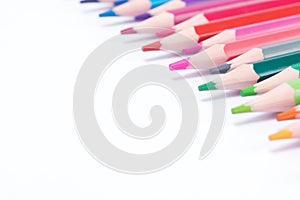 White background with multicolored, sharpened pencils in the form of a triangle, in the upper right corner