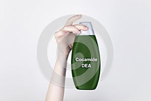 Chemical components on the shampoo label: Cocamide DEA. Female hands hold the jar on which indicates the harmful ingredient. White photo