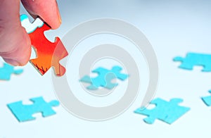 On a white background puzzles inside out. One red puzzle is held by female fingers in the left corner of the picture