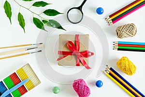 on a white background, a set of stationery, pencils, thread, paint brushes, plasticine and a gift with a red ribbon.