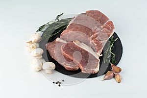 On a white background, on a slate board, there is a pork tenderloin with rosemary, garlic, pepper and mushrooms