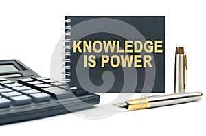 On a white background, there is a calculator, a pen and a black notebook with the inscription - KNOWLEDGE IS POWER