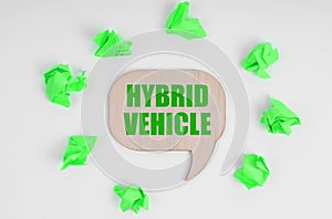 On a white background, there are crumpled green pieces of paper and a wooden sign with the inscription - Hybrid Vehicle