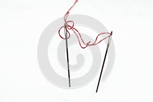 On a white background two sewing needles connected by a red thread