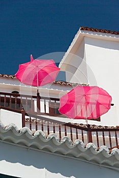 White balcony house with pink parasols on a background of blue sky