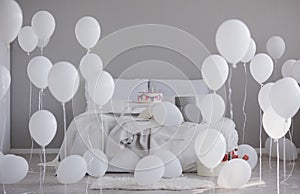 White balloons in grey bedroom interior with king size bed, real photo with copy space on the empty wall