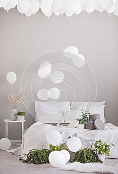 White balloons under the ceiling of grey scandinavian bedroom with double bed and green plants in pots, real photo with copy space