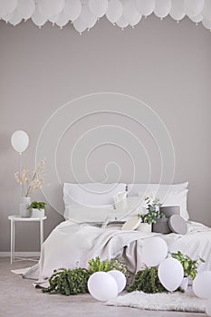 White balloons under the ceiling of stylish grey bedroom with comfortable bed, real photo with