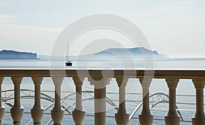 White balustrade overlooking the Bay, blue mountains and a boat with a mast.