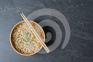 White bamboo plate bowl with egg noodles and chopsticks on a dark marble slate background
