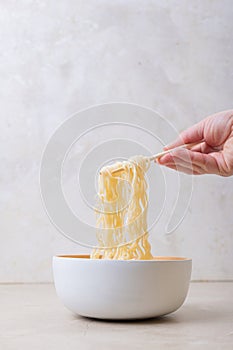 White bamboo plate bowl with egg noodles and chopsticks on a light background