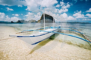 White banca boat on the sandy beach ready for island hopping trip. Amazing Pinagbuyutan island in background. Beautiful